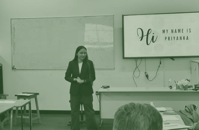 Priyanka presenting to a room, beside a screen that reads Hi, my name is Priyanka